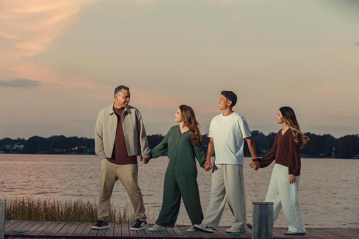 Gilmar, Aline, Nicolas e Maria de mãos dadas, caminhando num píer à beira do lago no fim da tarde