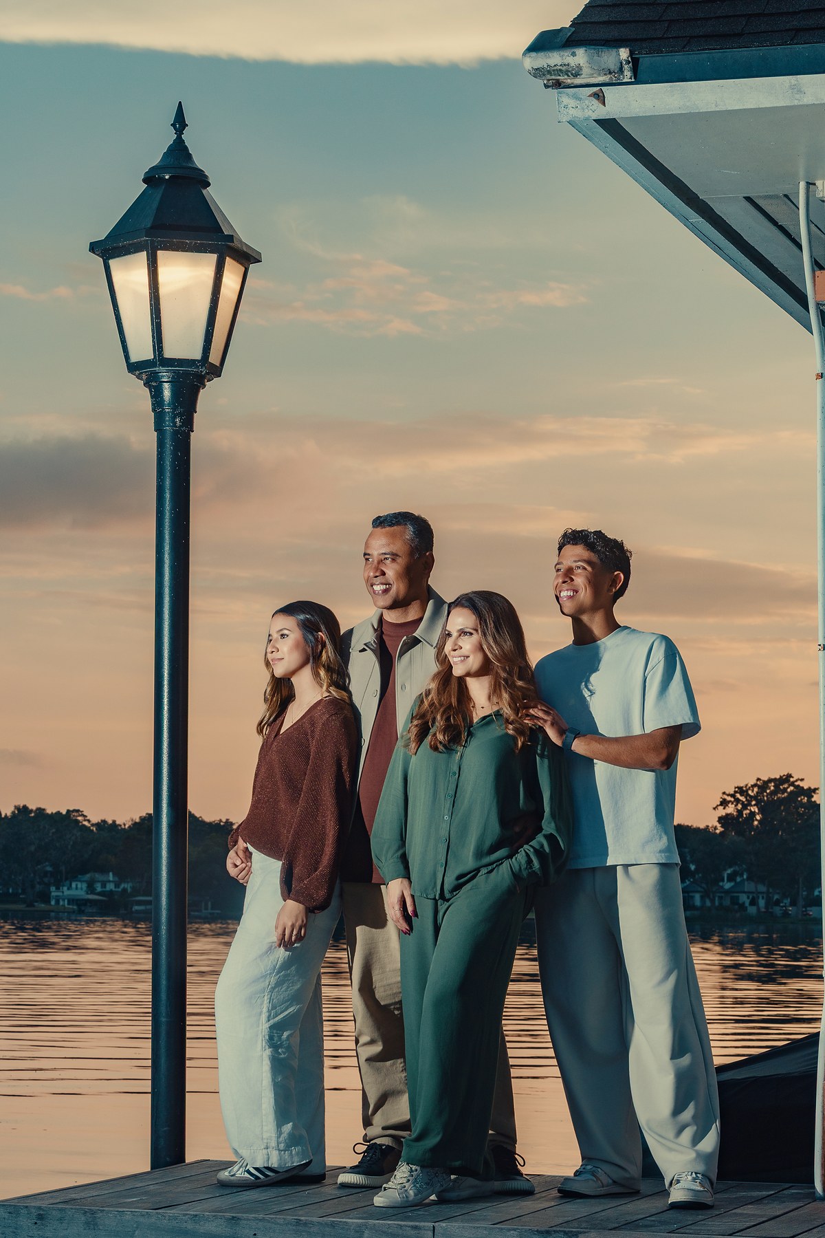 Gilmar, Aline, Nicolas e Maria num píer à beira do lago, ao lado de um poste aceso, no pôr do sol